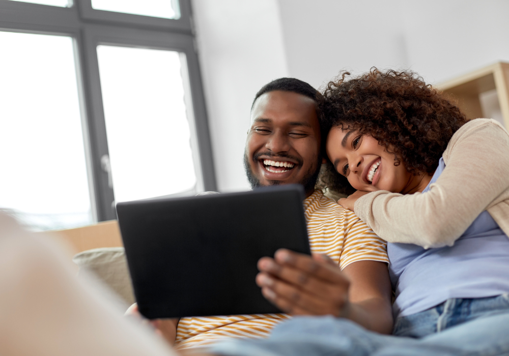 young black couple laughing looking at a tablet